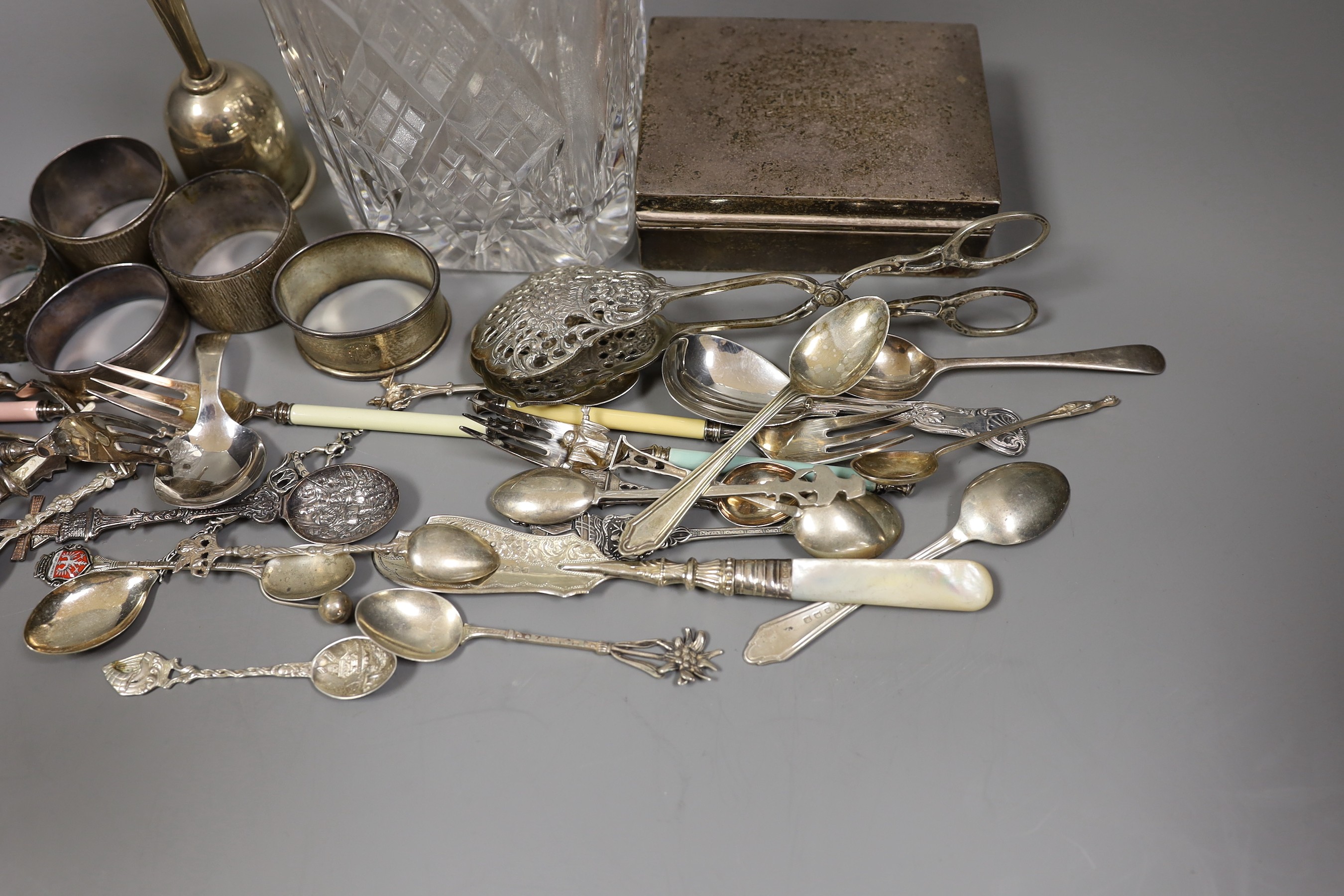 Mixed silver items etc. including a modern silver collared glass decanter, cigarette box, 800 standard white metal cake tongs, a white metal hand bell(lacking clapper), six plated Noritake tea forks, assorted minor silve